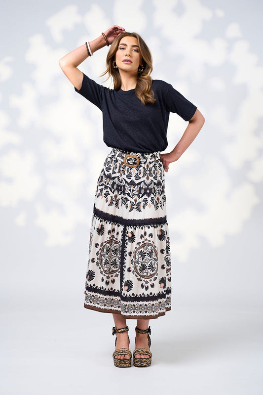 Woman wearing a black top and patterned skirt against a white background