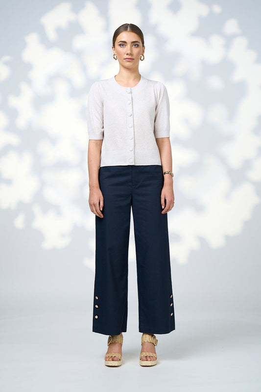 Woman wearing a white top and navy pants against a light background