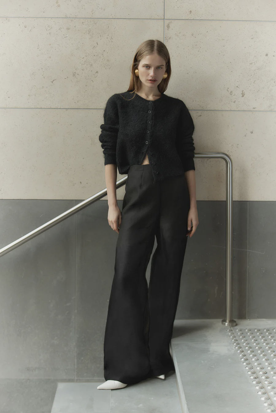 Woman wearing a black outfit standing against a minimalistic wall.