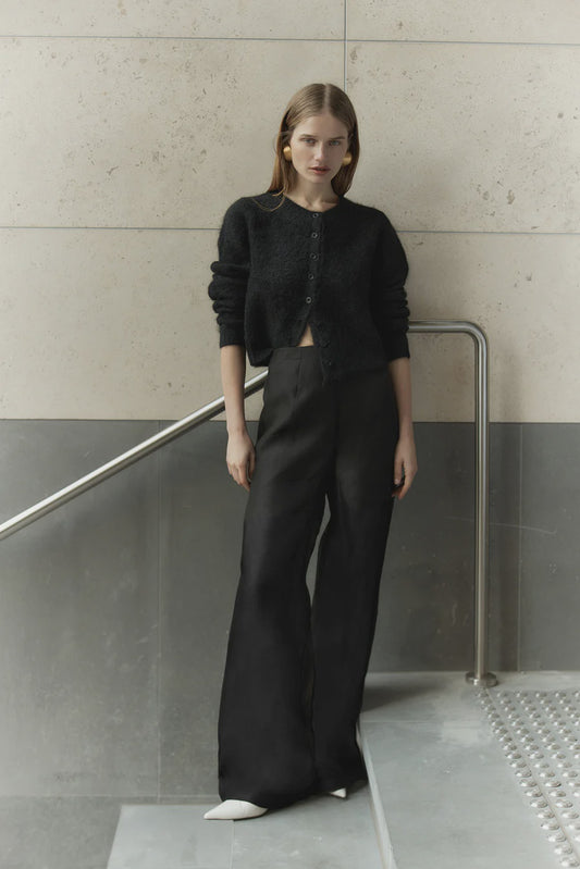 Woman wearing a black outfit standing against a minimalistic wall.