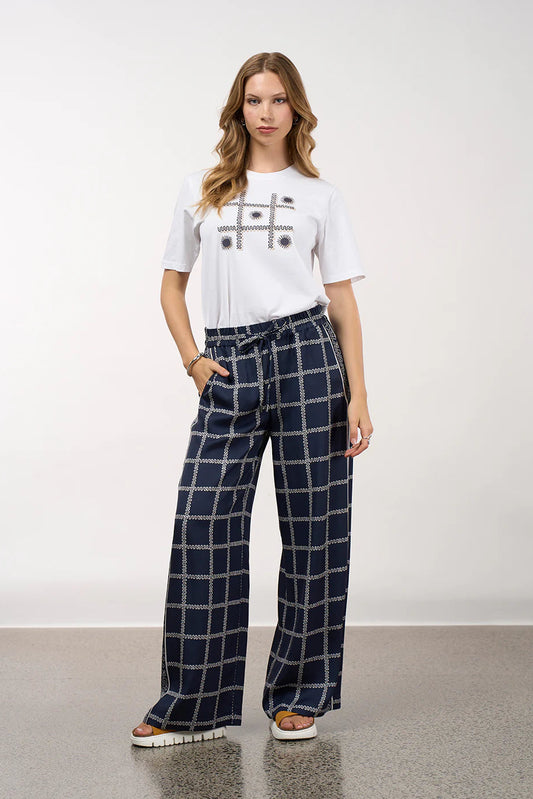 Woman wearing a white t-shirt with a graphic design and navy checkered pants on a plain background