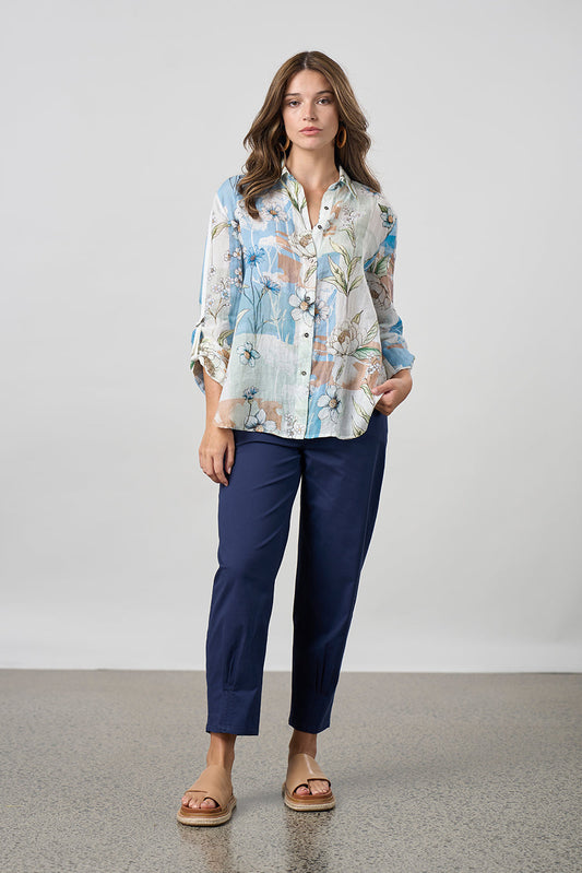 Woman wearing a patterned blouse and navy pants against a plain background
