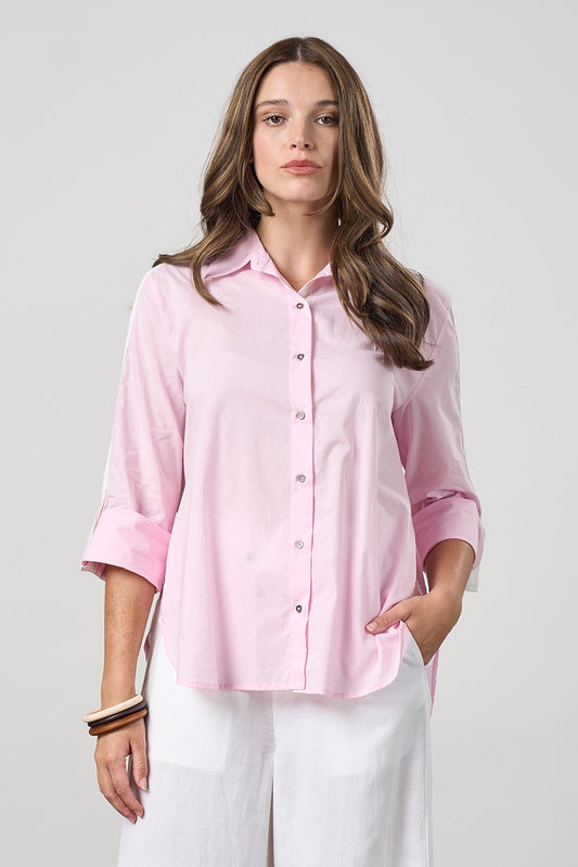 Woman wearing a pink button-up shirt and white pants on a light gray background