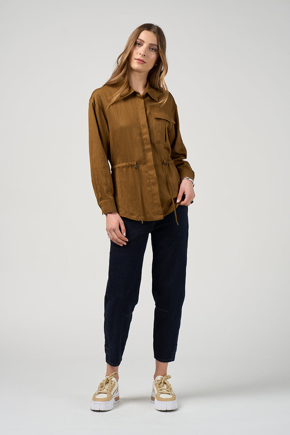 Woman wearing a brown jacket and navy pants on a white background