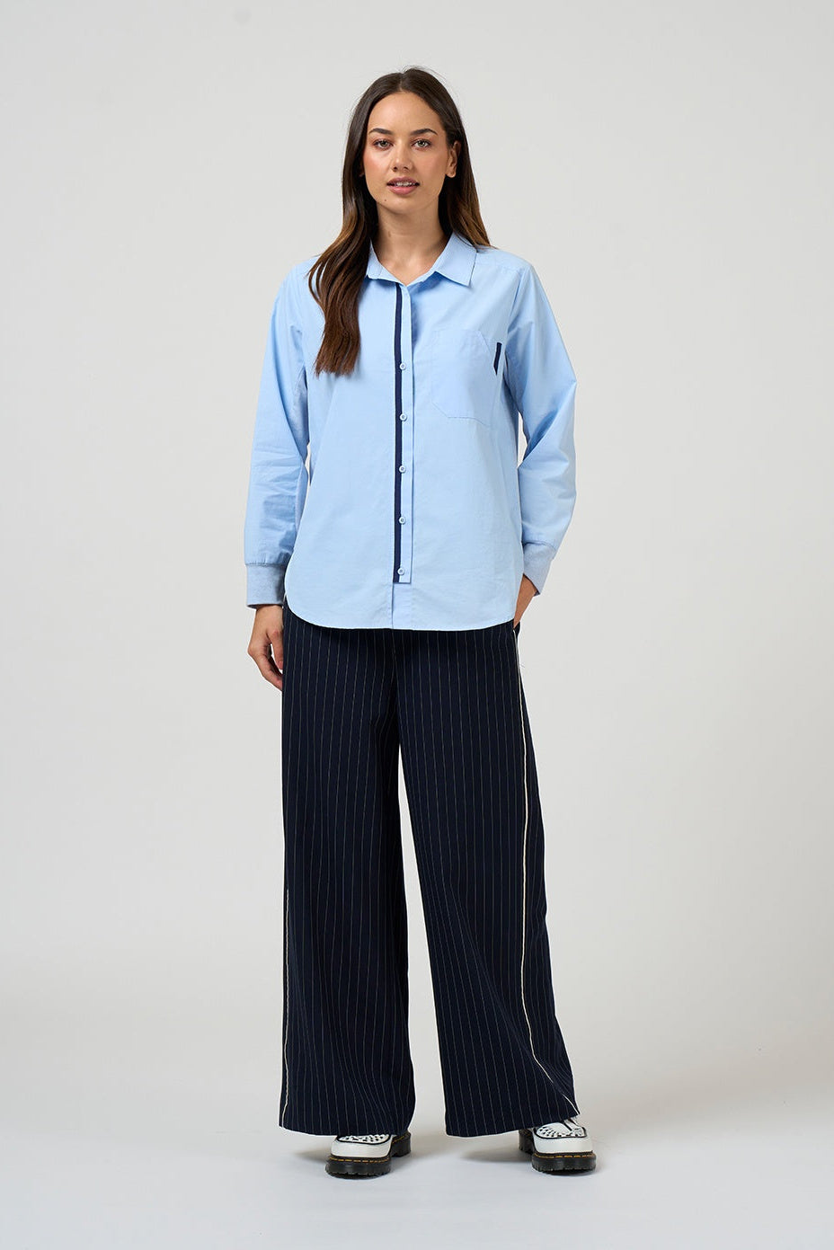 Woman wearing a light blue shirt and dark pinstripe pants on a white background