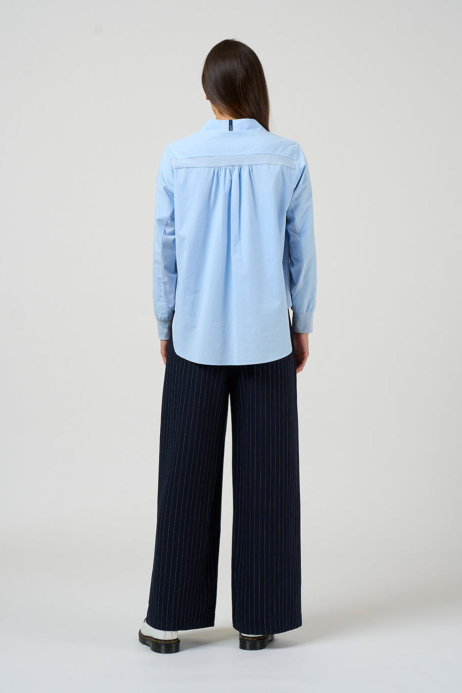 Person wearing a light blue shirt and dark pants on a white background