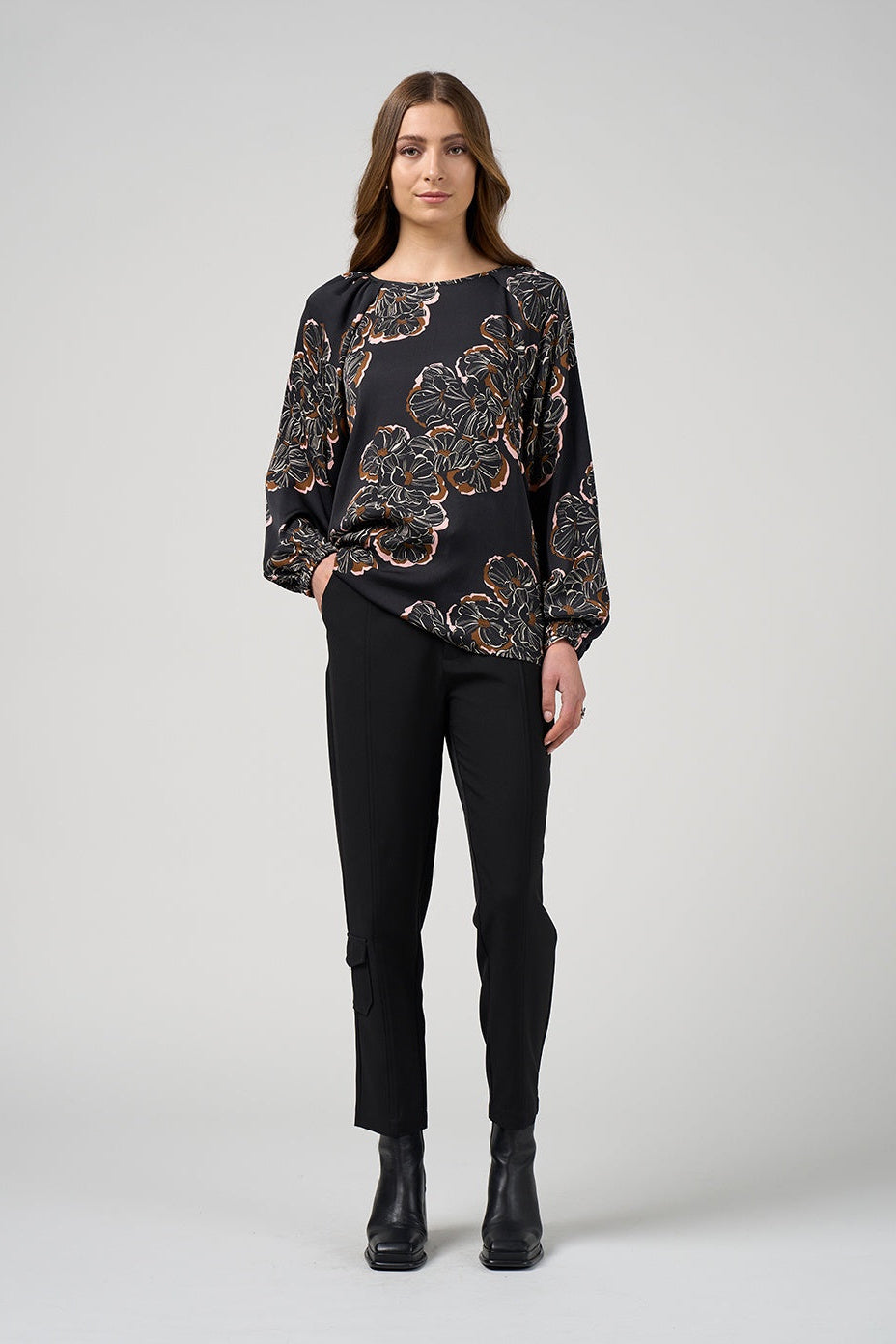 Woman wearing a black floral blouse and black pants on a white background