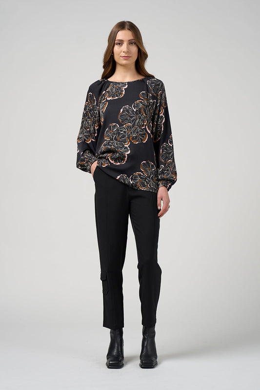 Woman wearing a black floral blouse and black pants on a white background