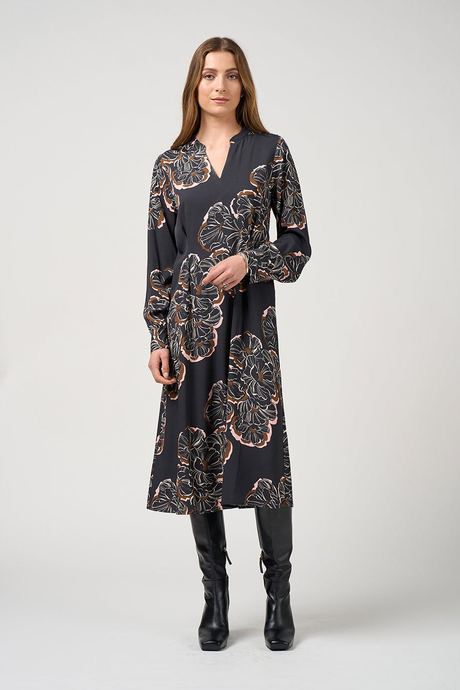 Woman wearing a black floral dress with black boots on a white background