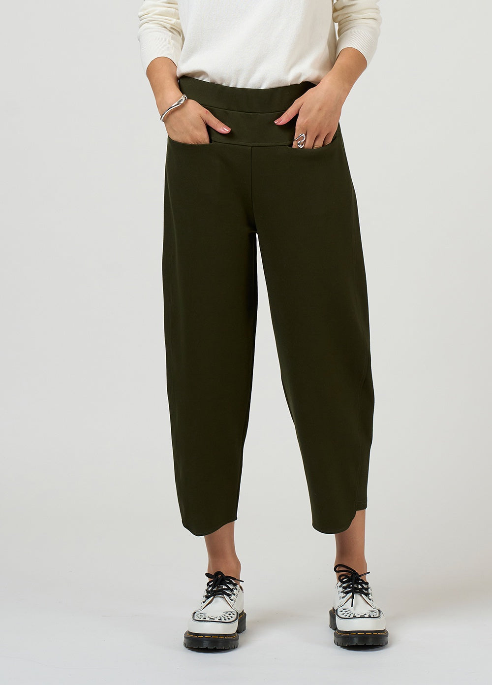 Person wearing dark green pants and white sneakers on a plain background