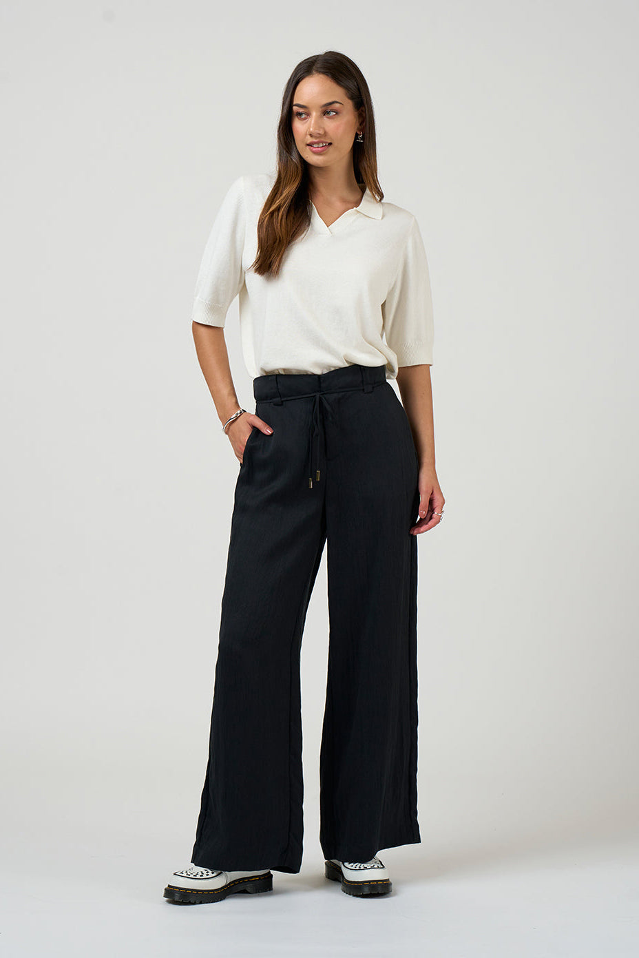 Woman wearing a white blouse and black wide-leg pants on a white background