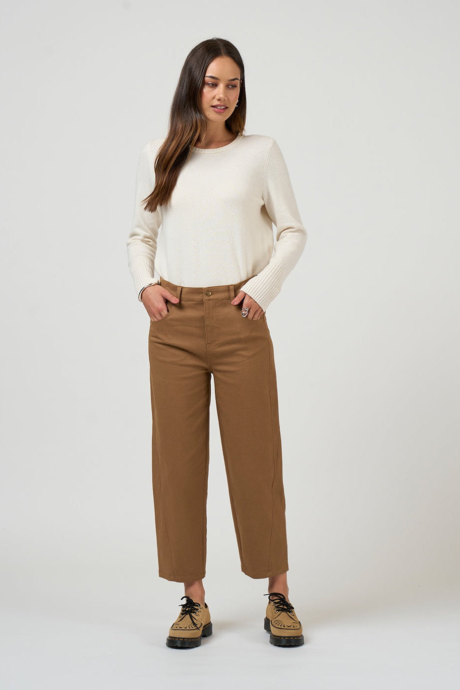 Woman wearing a cream sweater and brown pants on a white background