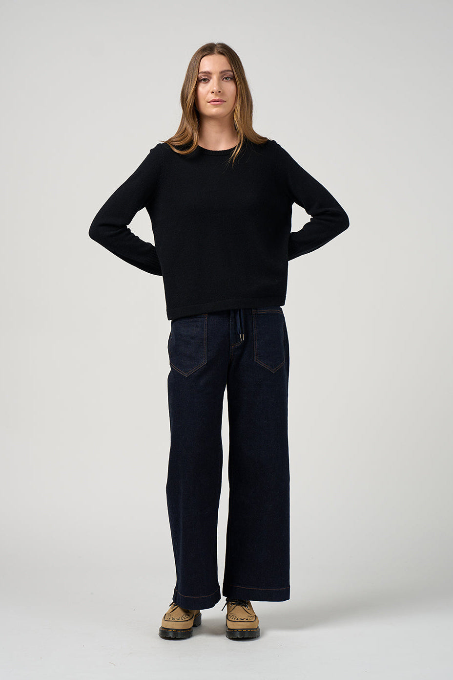 Person wearing a black sweater and dark pants on a white background