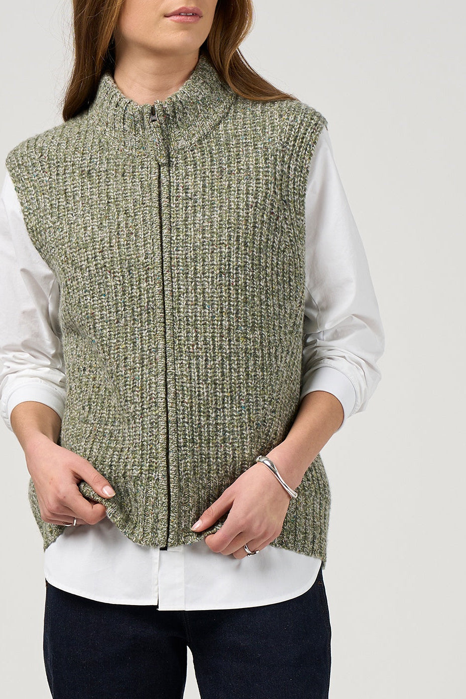 Person wearing a green knitted vest over a white shirt on a plain background
