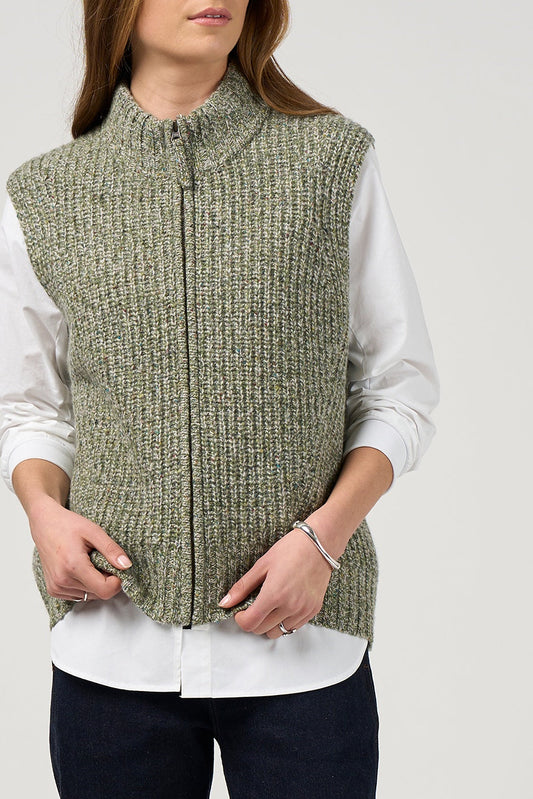 Person wearing a green knitted vest over a white shirt on a plain background