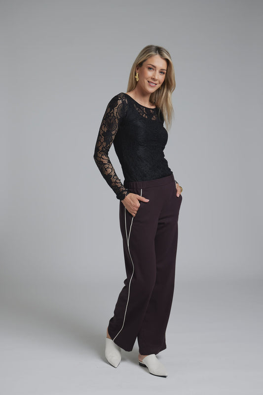 Woman wearing a black lace top and brown pants on a gray background