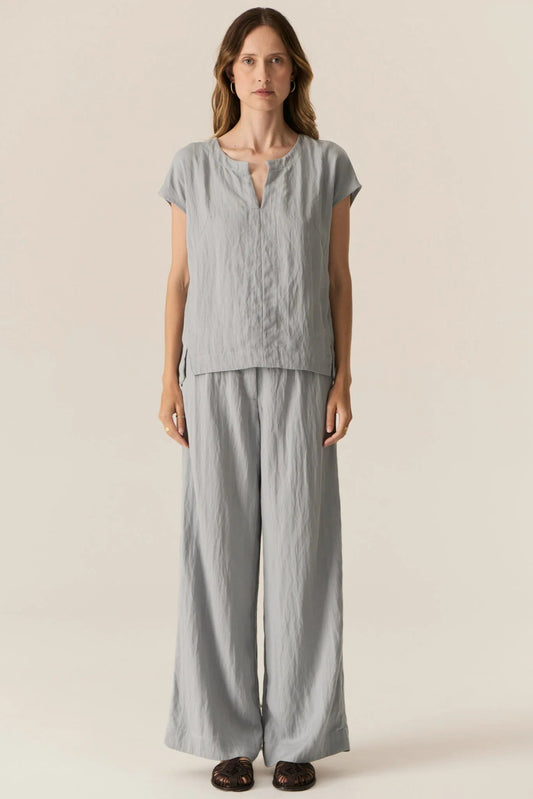 Woman wearing a light gray top and wide-leg pants on a beige background