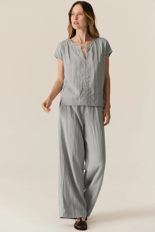 Woman wearing a gray outfit with a top and wide-leg pants on a beige background