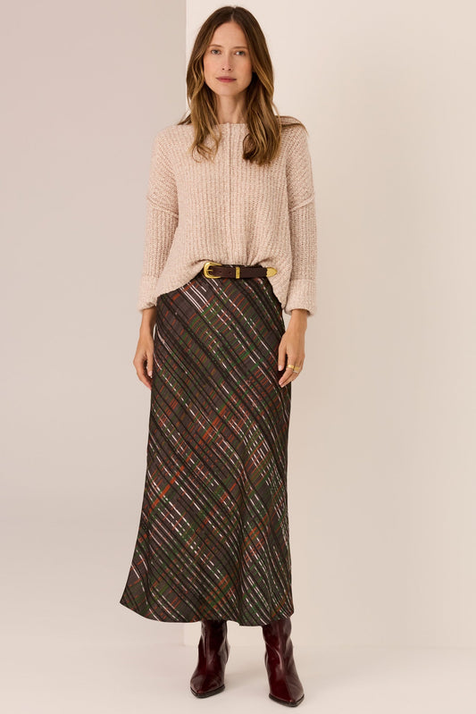 Woman wearing a beige sweater and plaid skirt on a plain background