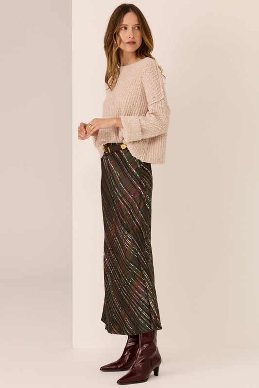 Woman wearing a beige sweater and patterned skirt on a plain background