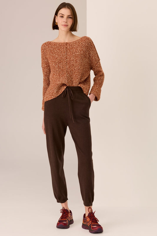 Woman wearing a brown knitted sweater and dark brown pants on a beige background