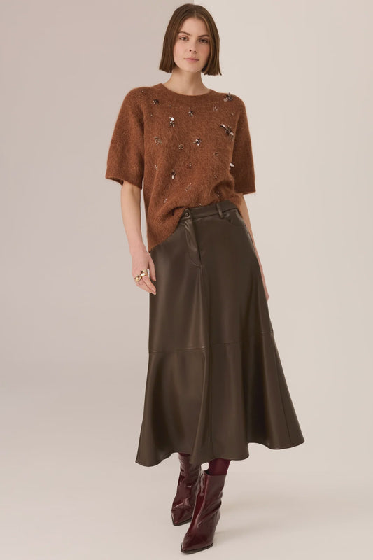 Woman wearing a brown sweater and dark brown skirt on a beige background
