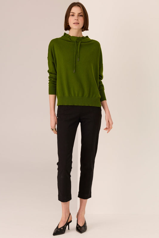 Woman wearing a green hoodie and black pants on a beige background