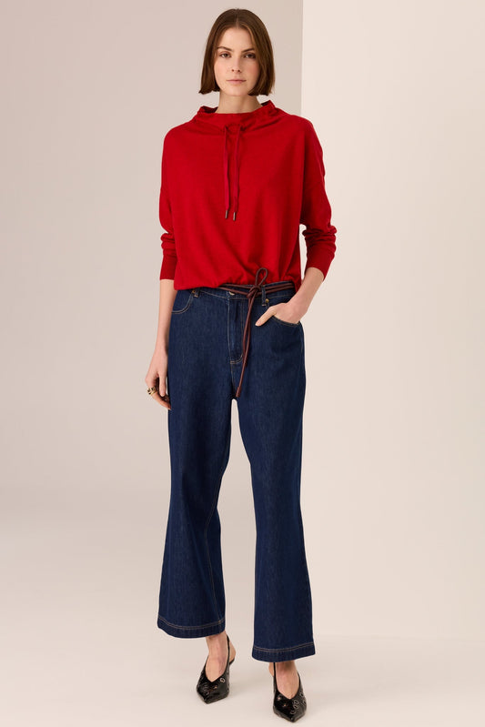 Woman wearing a red hoodie and blue jeans on a beige background