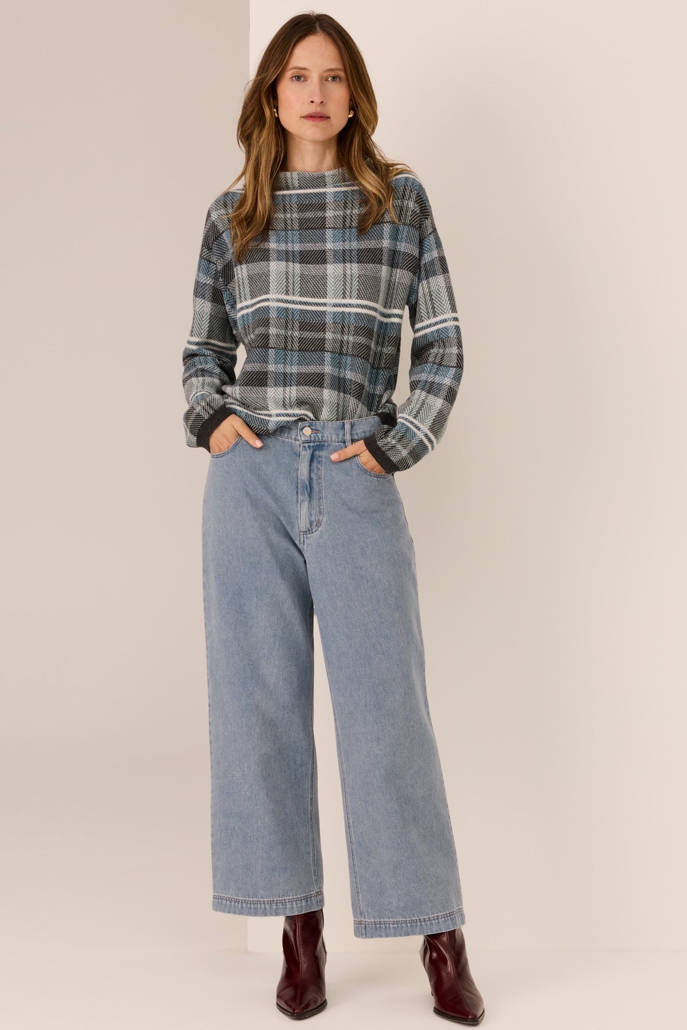 Woman wearing a plaid sweater and blue jeans on a plain background