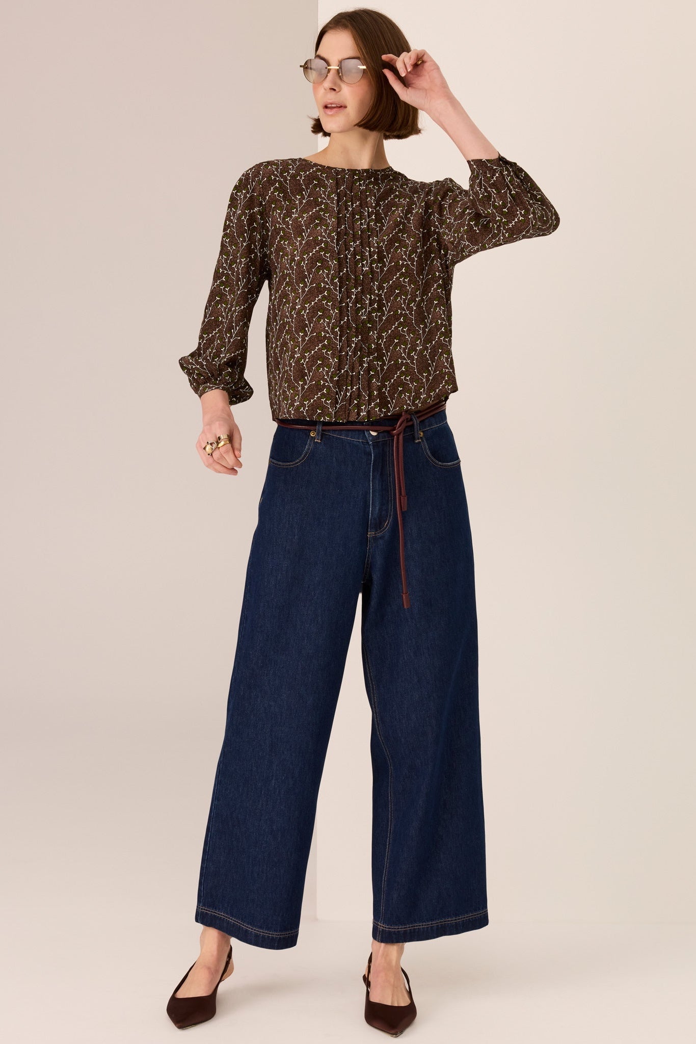 Person wearing a patterned top and blue jeans on a plain background