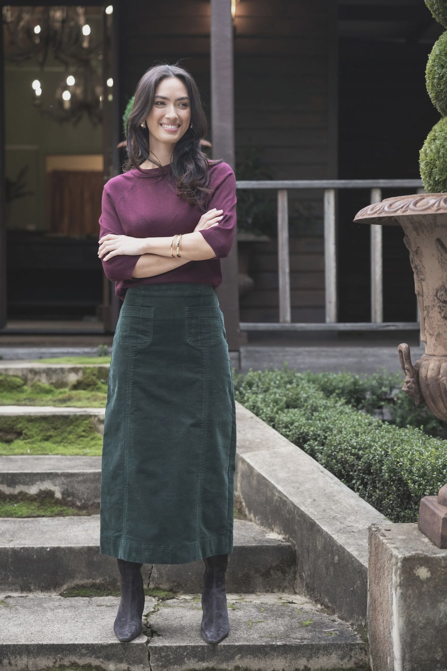 Woman standing on steps outdoors wearing a purple top and green skirt.
