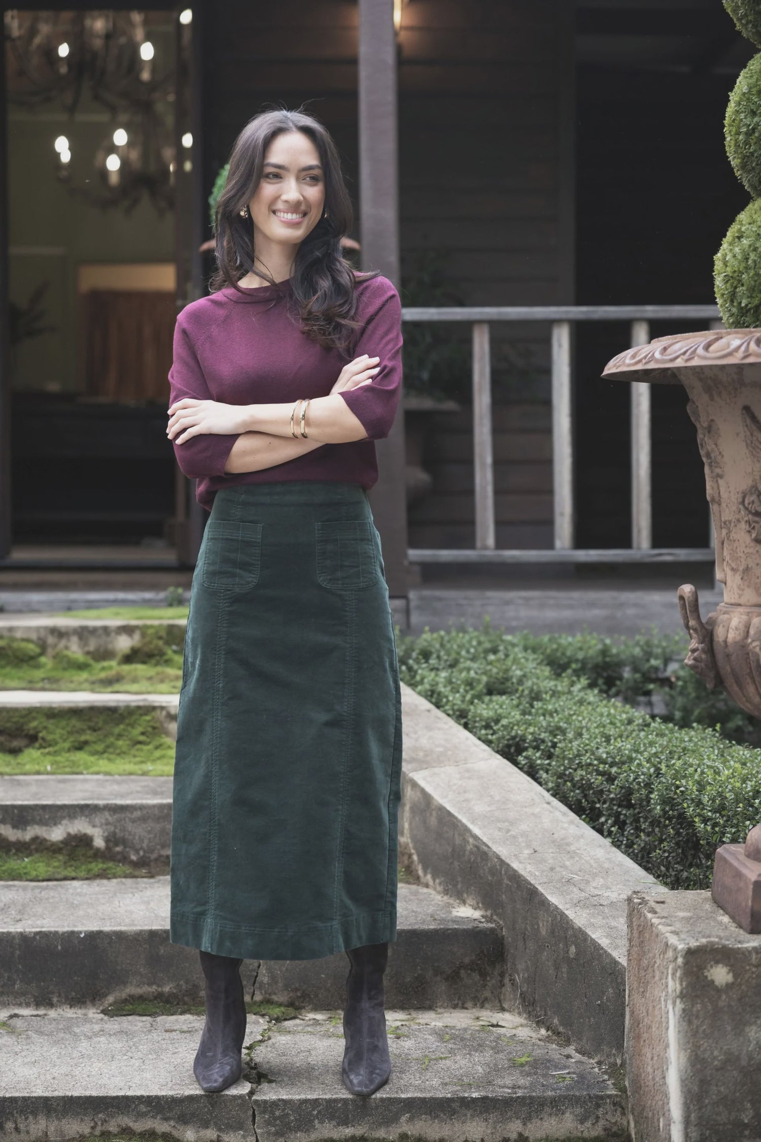 Woman standing on steps outdoors wearing a purple top and green skirt.