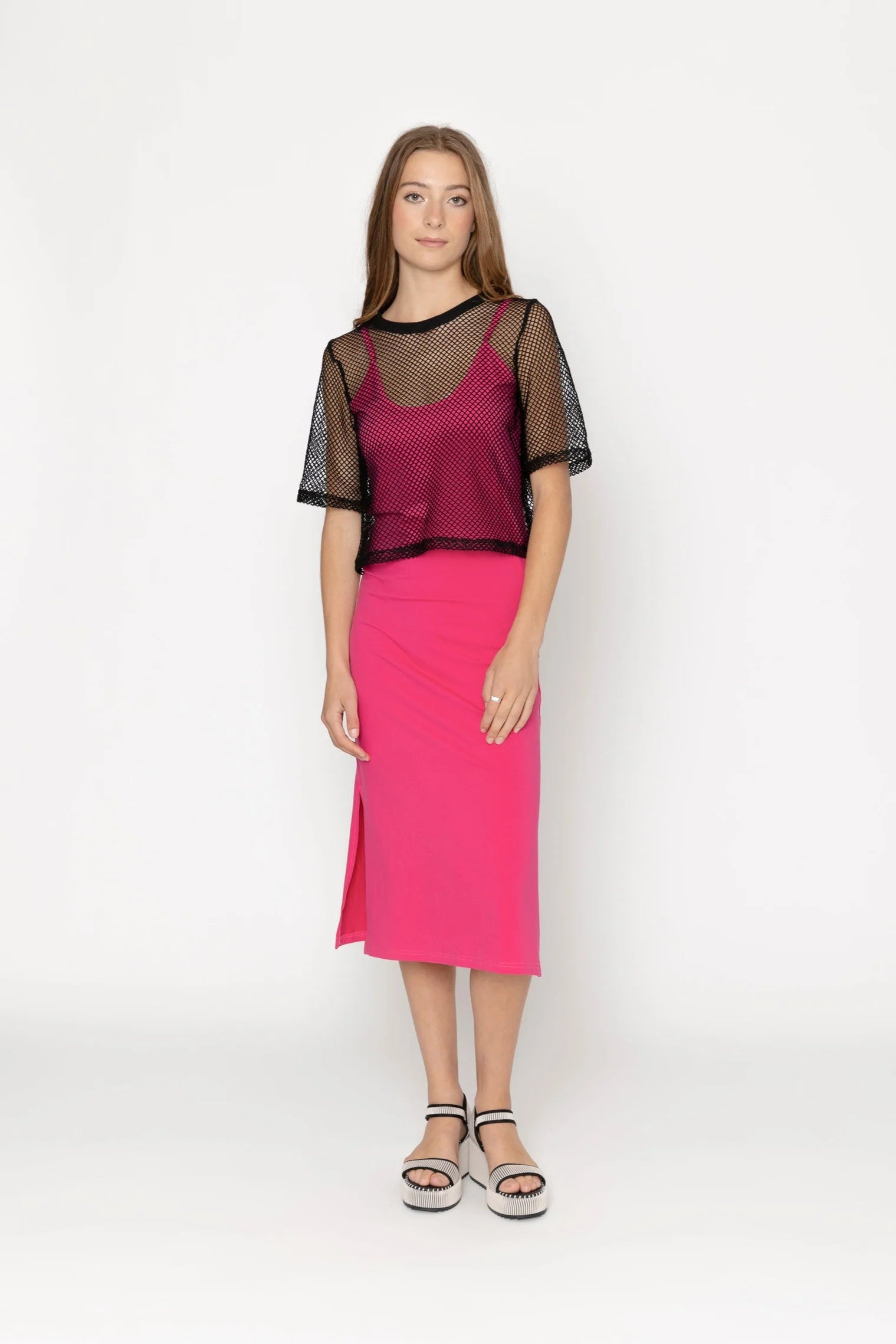 Woman wearing a pink skirt and black top with sheer sleeves on a white background