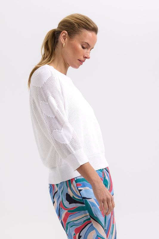 Woman wearing a white sweater and colorful pants on a light gray background