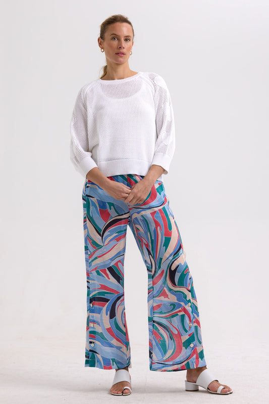 Woman wearing a white sweater and colorful patterned pants on a white background