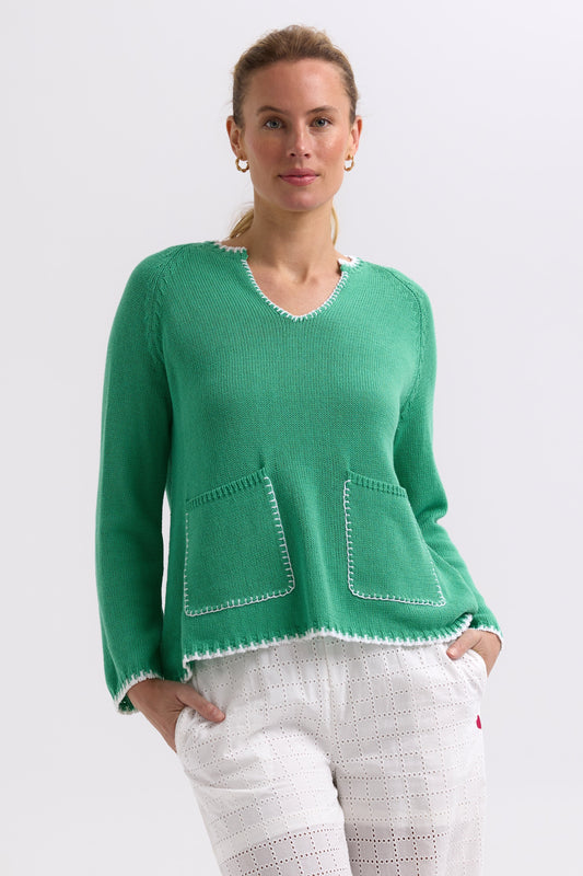 Woman wearing a green sweater with white trim on a plain background