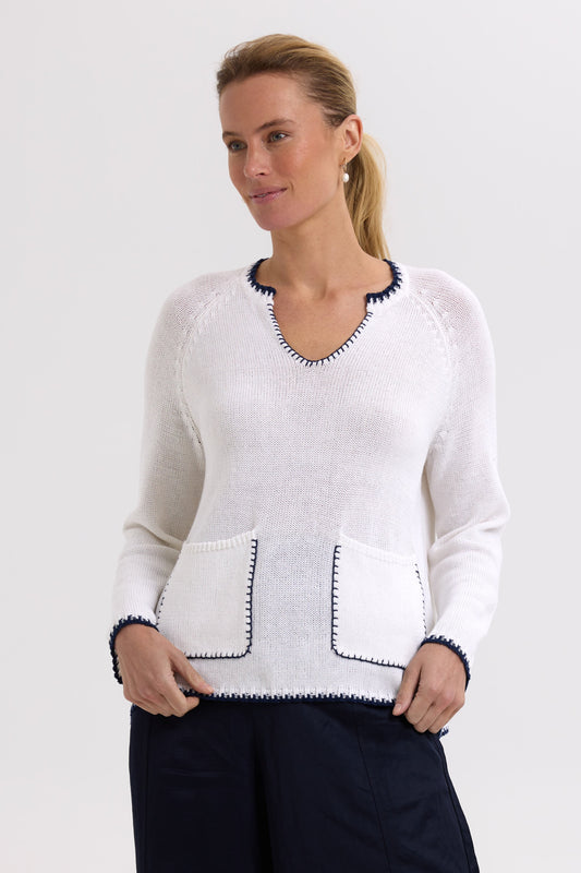 Woman wearing a white sweater with black accents on a plain background