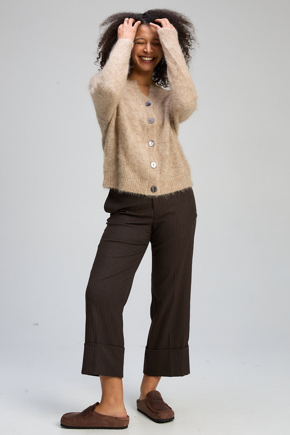 Woman wearing a beige sweater and brown pants on a white background