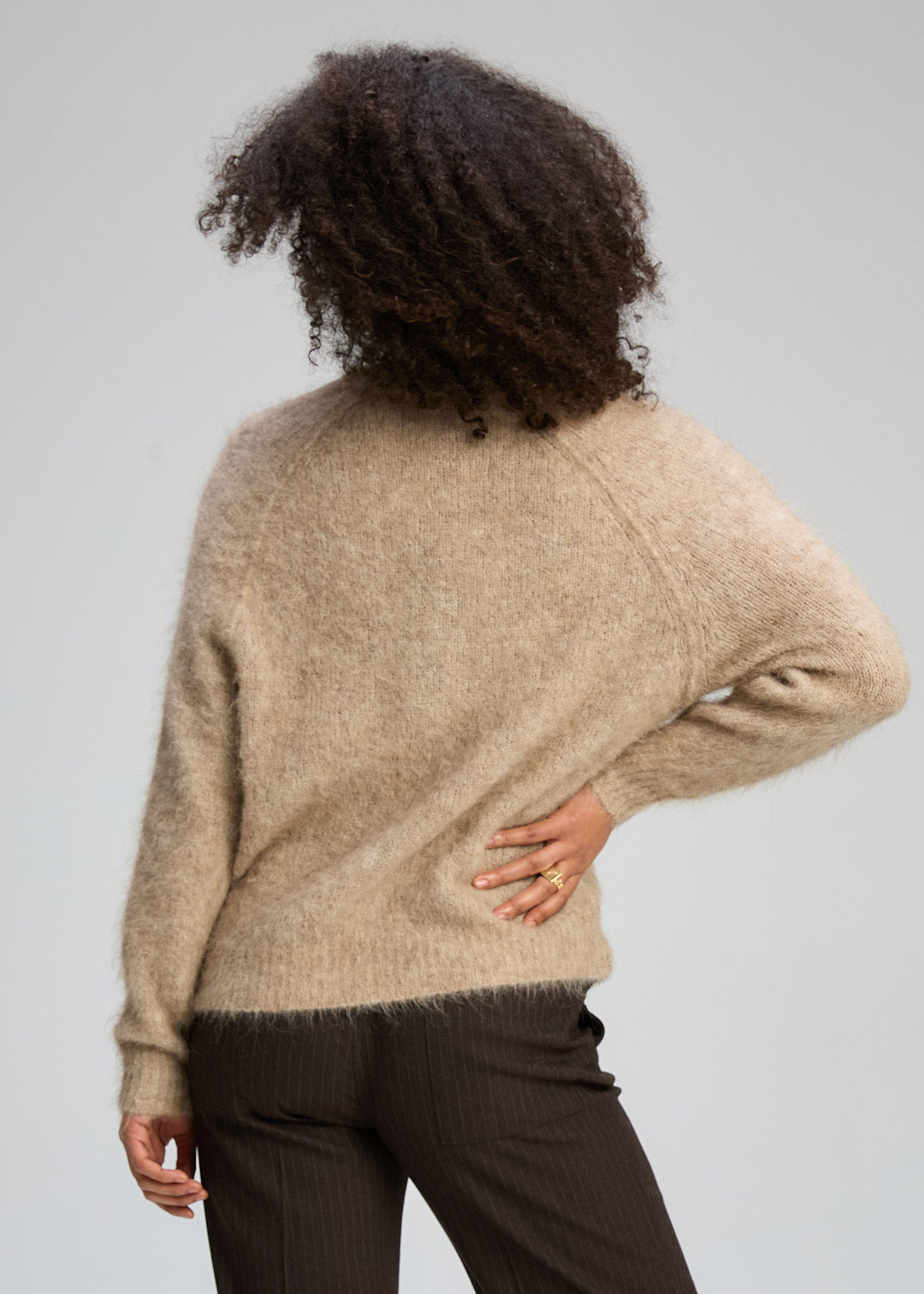 Person wearing a beige sweater and dark pants against a plain background