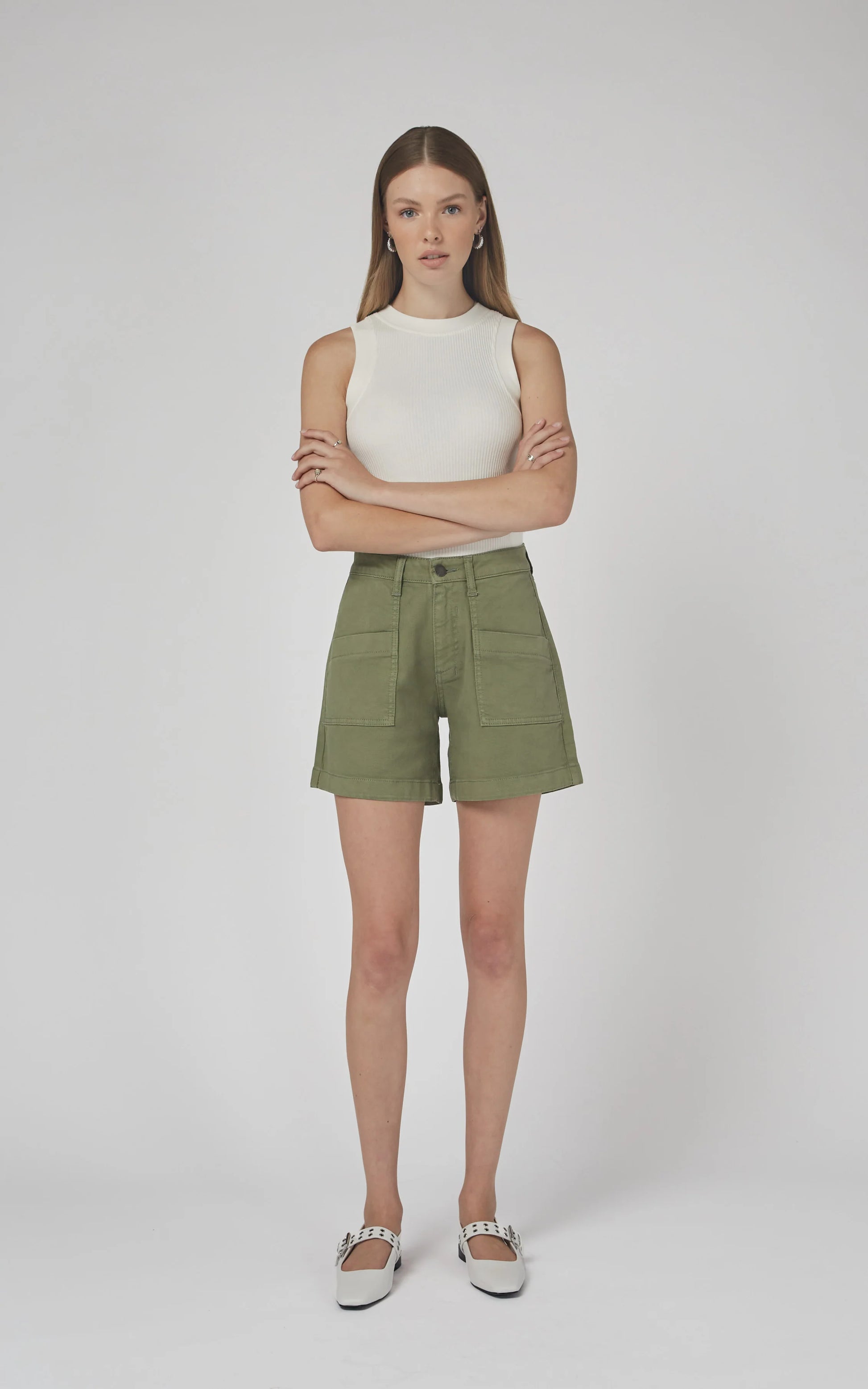 Woman wearing a white sleeveless top and green shorts on a plain background