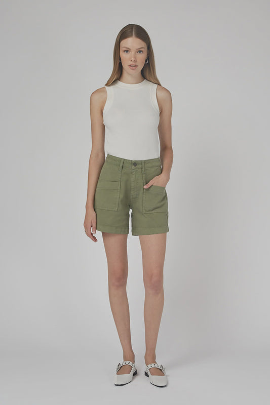 Woman wearing a white sleeveless top and green shorts on a plain background