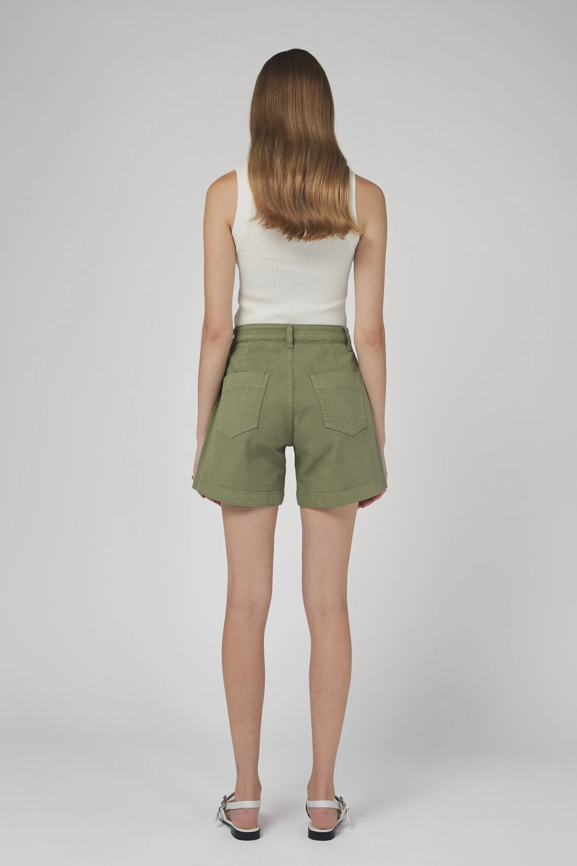 Woman wearing green shorts and a white top on a plain background