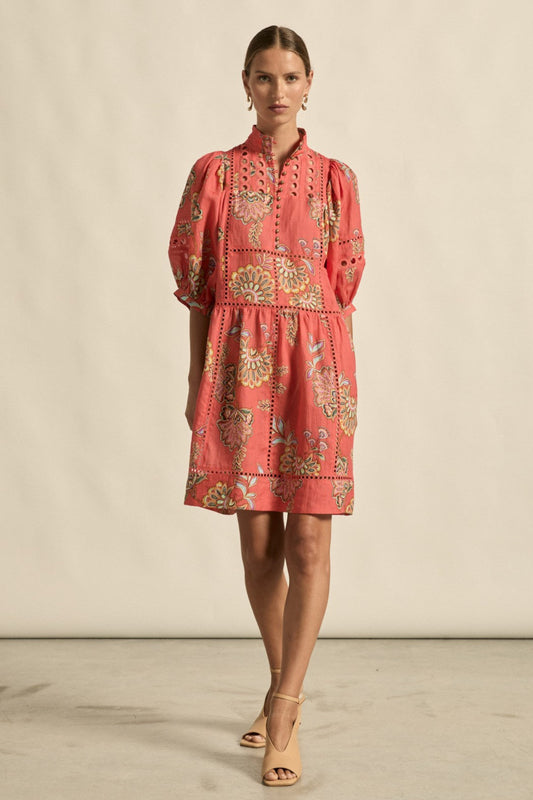 Woman wearing a coral dress with gold embroidery against a beige background