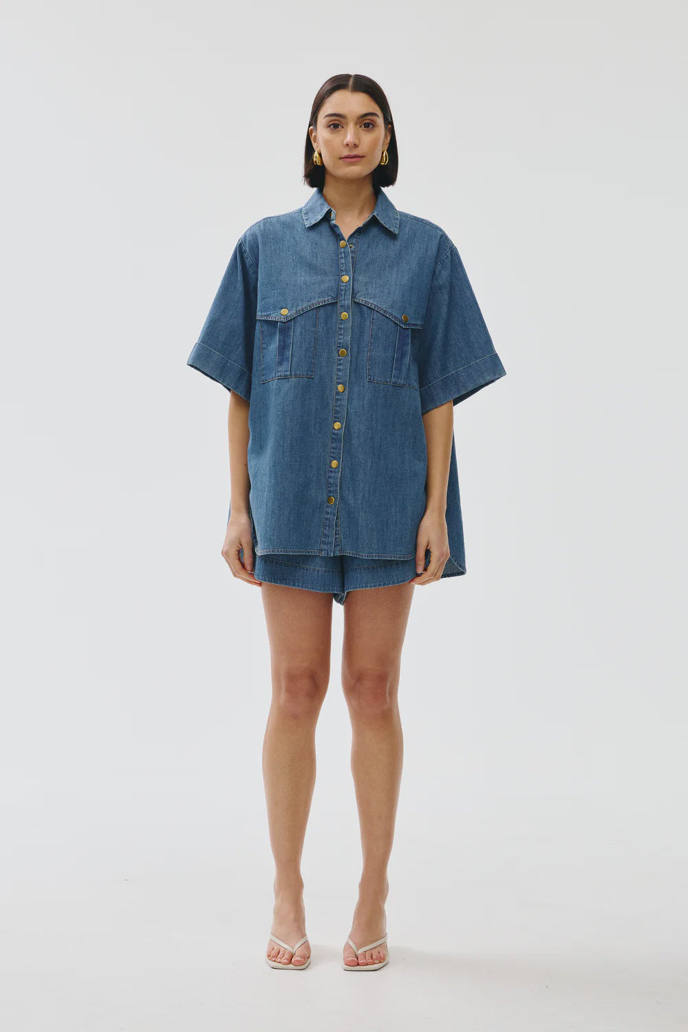 Person wearing a blue denim shirt and shorts on a white background
