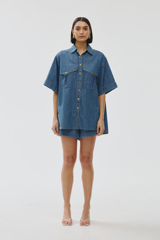Person wearing a blue denim shirt and shorts on a white background