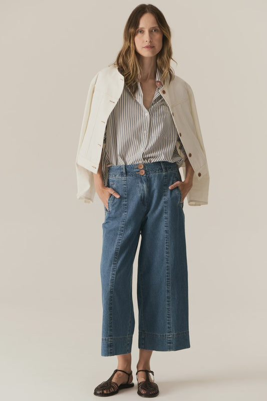 Woman wearing a white jacket, striped shirt, and blue jeans on a plain background