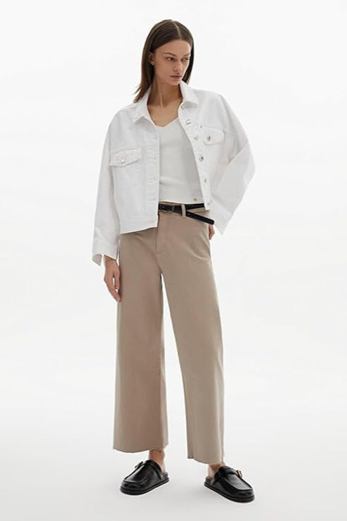 Woman wearing a white denim jacket, white shirt, beige pants, and black shoes on a white background