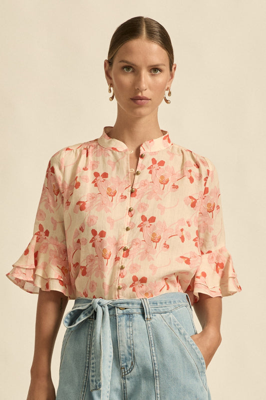 Woman wearing a floral blouse and denim pants against a beige background