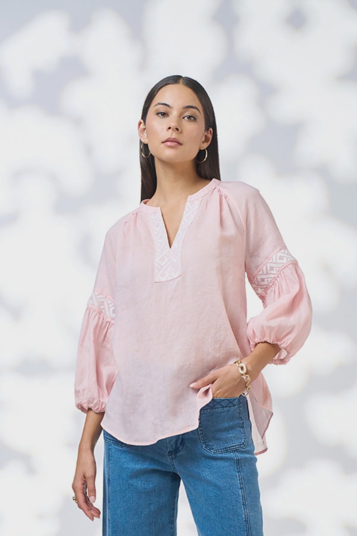 Woman wearing a pink blouse with lace details and blue jeans against a white background