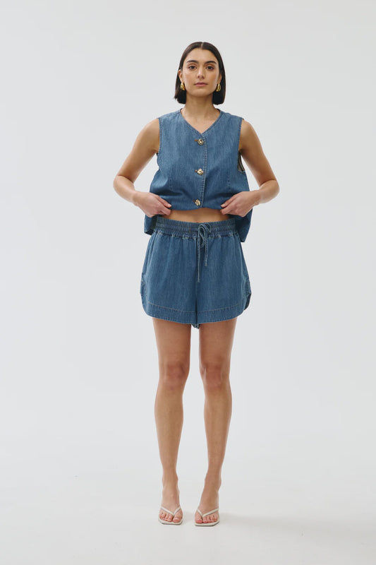 Woman wearing a denim sleeveless top and shorts on a white background